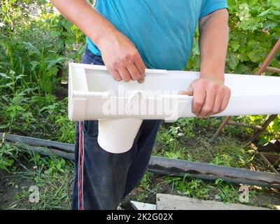 Construction de gouttières. Entrepreneur installant le tuyau de vidange de la goulotte de descente de gouttière. Banque D'Images