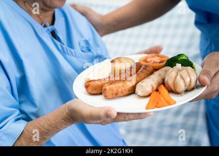 Les personnes âgées ou vieille femme malade manger le petit déjeuner des aliments sains avec espoir et professionnels tout en restant assis sur le lit de la faim et à l'hôpital. Banque D'Images