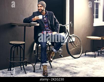 Commencez votre journée correctement avec une tasse de café. Photo d'un beau jeune homme en train de savourer une tasse de café dans un café de la ville pendant que son vélo se tient à côté de lui. Banque D'Images