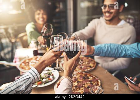 Merci à tous d'être venu. Photo d'un groupe de jeunes amis joyeux ayant un toast festif avec du vin au dîner à l'intérieur d'un restaurant. Banque D'Images