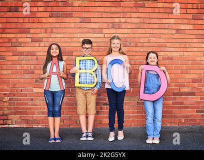 Plus vous en savez, plus vous vous développez. Portrait d'un groupe de jeunes enfants tenant des lettres de l'alphabet contre un mur de briques. Banque D'Images