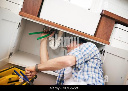 Je pense que je vois votre problème. Photo d'un homme fixant un tuyau sous son évier de cuisine. Banque D'Images