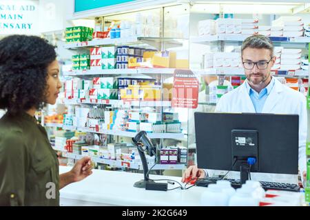 Extraction. Plan court d'un beau pharmacien d'âge mûr aidant une cliente de sexe féminin à la pharmacie. Banque D'Images