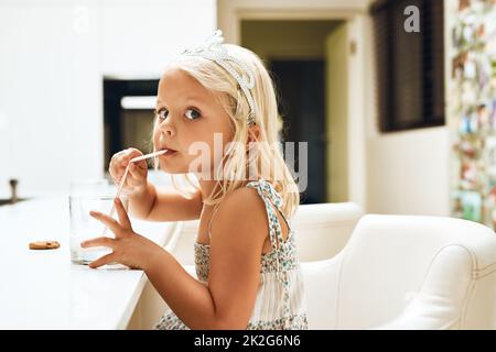 S'en déleffet. Portrait d'une adorable petite fille qui boit du lait dans un verre à la maison. Banque D'Images