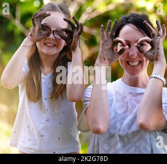 Jouez ensemble. Restez ensemble. Portrait d'une mère et de sa petite fille couvrant leurs yeux avec leurs mains boueuses dehors. Banque D'Images