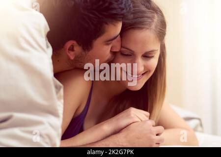 Chaque baiser se sent comme le premier. Photo d'un jeune couple aimant partageant un baiser tout en étant allongé sous une couverture ensemble. Banque D'Images