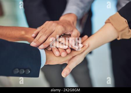 Réunis-nous et faisons fonctionner cette tâche. Gros plan d'un groupe d'hommes d'affaires méconnus qui forment un caucus avec leurs mains en se tenant au bureau pendant la journée. Banque D'Images