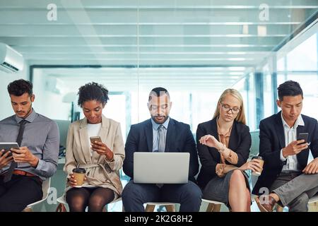 Attendre patiemment leur tour. Photo d'un groupe de jeunes hommes d'affaires assis ensemble sur des chaises et prenant des notes en utilisant différentes méthodes tout en attendant dans le bureau pendant la journée. Banque D'Images