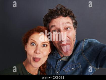 Légèrement goofy. Portrait d'un jeune couple heureux tirant des visages stupides pour un selfie. Banque D'Images