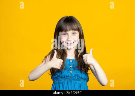 Une petite fille souriante a levé son pouce vers le haut et montre Cool, Super. Dents de lait perdues dans la bouche. Concept de dentiste. Isolé sur fond jaune. Banque D'Images