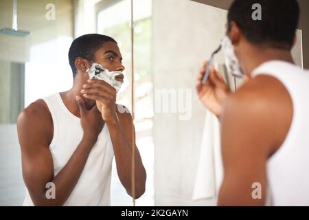 Se débarrasser des poils tenaces. Un jeune homme se raser dans le miroir. Banque D'Images