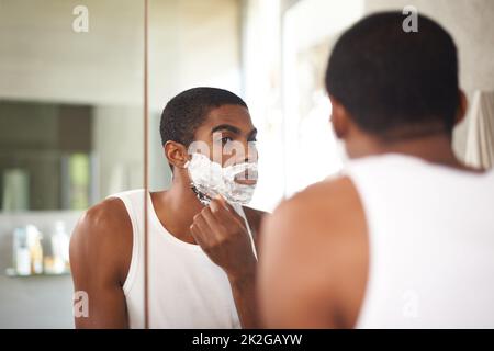 Se débarrasser des poils tenaces. Un jeune homme se raser dans le miroir. Banque D'Images