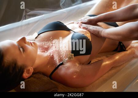 Une peau éclatante est à quelques pas. Photo d'une femme qui reçoit un gommage au sel dans un spa. Banque D'Images