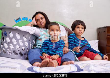 Tout cela se délaça un peu. Portrait d'une mère assise sur un lit avec ses deux fils. Banque D'Images