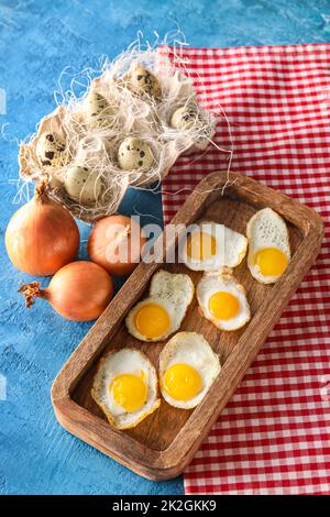 Panneau en bois avec œufs de caille frits et oignon sur fond de couleur Banque D'Images