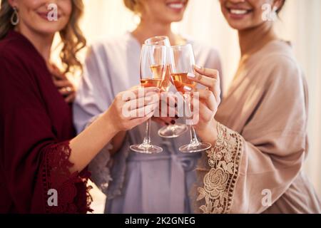 Santé à la mariée. Photo courte d'une mariée méconnue et de ses demoiselles d'honneur qui font un toast avec des lunettes de vin dans leur dressing avant le mariage. Banque D'Images