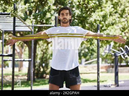 Réchauffer le corps. Photo d'un jeune homme utilisant son bracelet de résistance à l'extérieur du parc. Banque D'Images