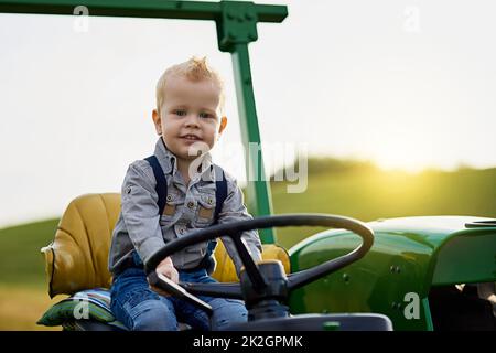 Grandir avec de bonnes valeurs agricoles à l'ancienne. Portrait d'un adorable petit garçon à bord d'un tracteur sur une ferme. Banque D'Images