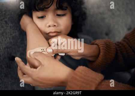 Maman est toujours là pour améliorer les choses. Plan d'une femme mettant un plâtre avec un visage triste dessiné sur le coude de ses fils. Banque D'Images