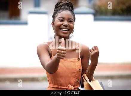 Je magasiner, donc je suis. Photo d'une jeune femme et montrant un signe de pouce vers le haut dans la ville. Banque D'Images