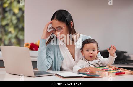 Être une mère est un travail dur. Photo d'une jeune mère qui a l'air stressée en travaillant à domicile. Banque D'Images