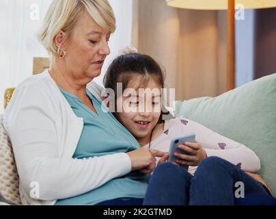 Pouvez-vous télécharger ce jeu pour moi, gran. Photo d'une petite fille utilisant un téléphone portable tout en étant assise à la maison avec sa grand-mère. Banque D'Images