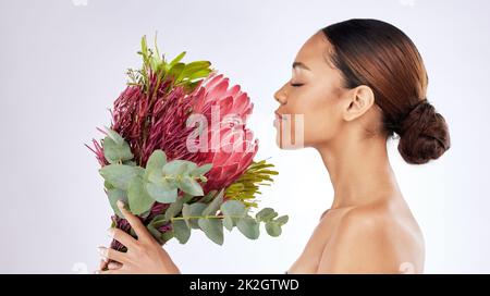 Arrêtez-vous et sentez les fleurs. Photo d'une jeune femme qui sent un bouquet de fleurs sur fond de studio. Banque D'Images