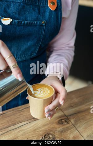 Processus consistant à préparer un cappuccino Barista avec un joli motif sur la mousse dans un verre éco-artisanal. Concept café à emporter. Banque D'Images