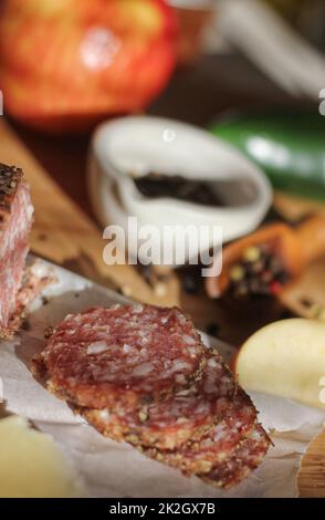 Salami au poivre sur plateau avec fromage anglais et irlandais, pommes en tranches et épices dans la cuisine rustique Banque D'Images