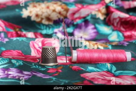 Filet avec aiguille et fil rose sur tissu satiné à motif fleuri d'époque Banque D'Images