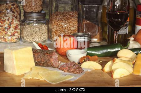 Salami au poivre sur plateau avec fromage anglais et irlandais, pommes en tranches et épices dans la cuisine rustique Banque D'Images