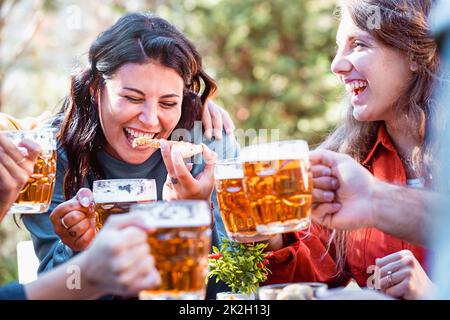 happy friends drinking beers and eating pizza outdoors and laughing together - focus on a young woman biting a slice of pizza - cheerful people, food Banque D'Images