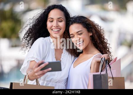 Les amis ne laissent pas leurs amis magasiner seuls. Photo de deux jeunes femmes prenant des selfies tout en faisant du shopping dans un environnement urbain. Banque D'Images