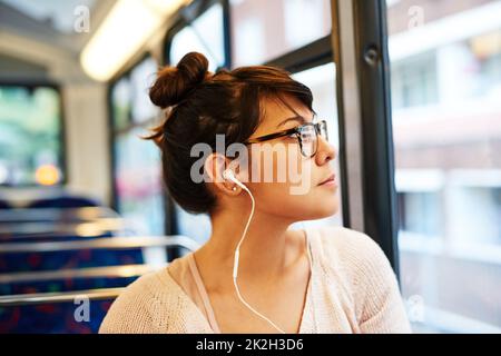 En prenant la vue sur son trajet en bus. Prise de vue rognée d'une jeune femme attrayante écoutant de la musique tout en étant assise dans un bus. Banque D'Images