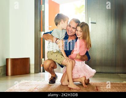 Bienvenue à la maison, papa. Prise de vue en longueur d'un homme mûr saluant ses enfants à la porte d'entrée après être arrivé à la maison de travail. Banque D'Images