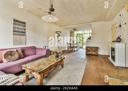 Corner sofa with soft cushions located under elegant chandelier near electric fireplace in light living room near kitchen Stock Photo