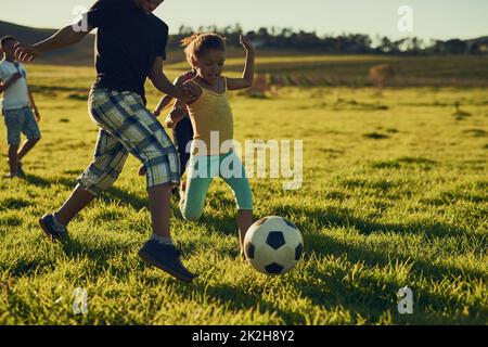 Amusez-vous avec vos amis et un ballon de football. Photo d'un groupe d'enfants jouant au football ensemble dans un champ à l'extérieur. Banque D'Images