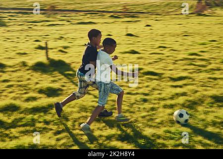 Le football s'amuse avec un ami. Prise de vue d'un deux enfants jouant au football ensemble dans un champ à l'extérieur. Banque D'Images