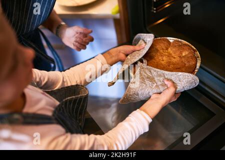 Un bonheur fait maison au four. Coupe courte d'une petite fille en retirant un gâteau fraîchement cuit du four à la maison. Banque D'Images