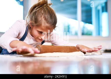 Shes un petit boulanger dans la fabrication. Coupe courte d'une petite fille qui roule de la pâte tout en faisant cuire à la maison. Banque D'Images