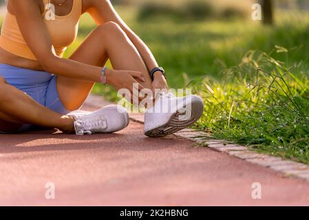 Gros plan d'une femme de 20s sur une piste de course à pied avec des hauts jaunes et des collants bleus tenant sa cheville dans la douleur. Banque D'Images