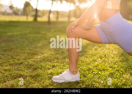 Gros plan d'Une femme avec un collant bleu qui s'étire les jambes et se réchauffe dans un parc public le matin. Banque D'Images