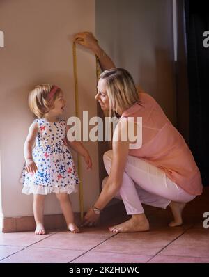 Vous avez grandi si vite. Photo d'une mère mesurant sa taille de petite fille à la maison. Banque D'Images