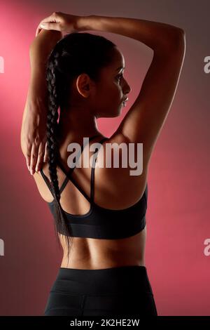 Vous devez vous étirer avant et après. Photo studio d'une jeune femme sportive qui étire les bras sur un fond rouge. Banque D'Images