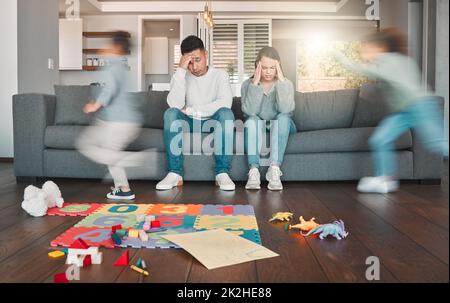 Besoin d'une pause. Photo de deux jeunes parents qui ont l'air fatigués pendant que leurs enfants courent à la maison. Banque D'Images