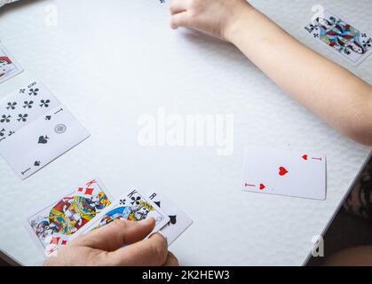 Gros plan de la main d'un homme et d'un enfant présentant des cartes à jouer sur une table blanche, le concept d'apprendre à jouer des cartes Banque D'Images