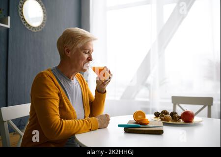 Femme souriante aux cheveux gris tenant un verre de jus Banque D'Images