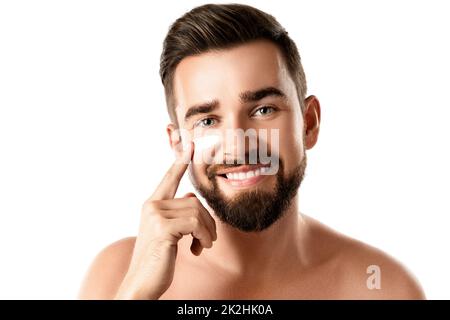 Le jeune homme applique de la crème hydratante et anti-âge sur son visage Banque D'Images