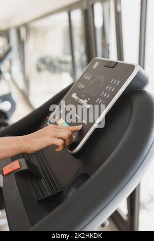 Femme changeant de réglages sur un tapis roulant dans une salle de gym Banque D'Images