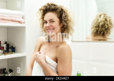 Belle femme aux cheveux bouclés après une douche dans une salle de bains Banque D'Images